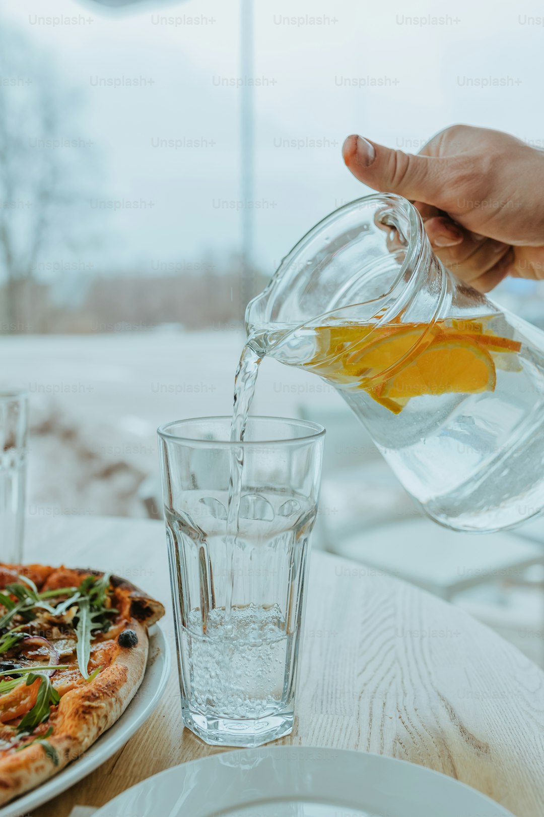 a person pours water from a pitcher into a glass