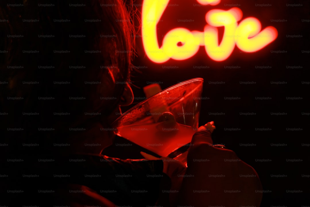 Person drinks cocktail near neon love sign
